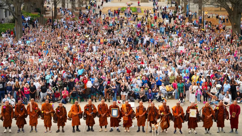 **Caption:**
“A vast crowd walking alongside a group of monks during the Walk for Peace, showing collective commitment to unity and nonviolence.”

**Alt text (SEO-optimized):**
“Large crowd and group of Buddhist monks walking together in the Walk for Peace, symbolizing mass participation, harmony, and peaceful coexistence.”